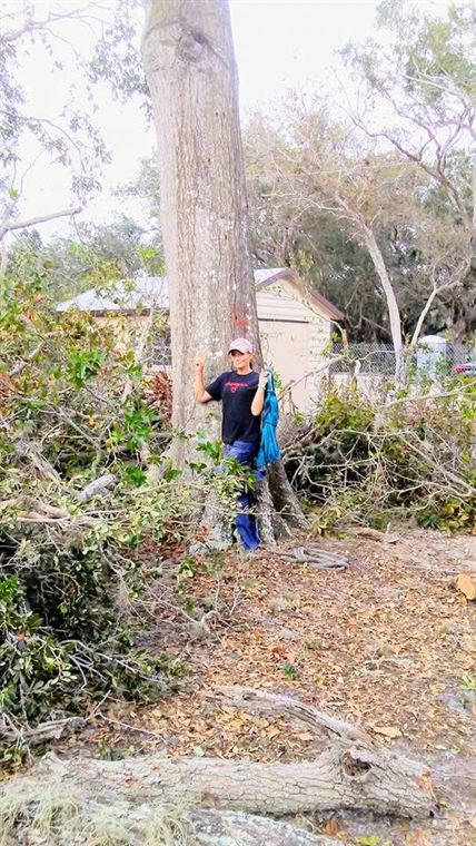 Jenniffer standing beside a large tree trunk, pointing up into what is left of the canopy.